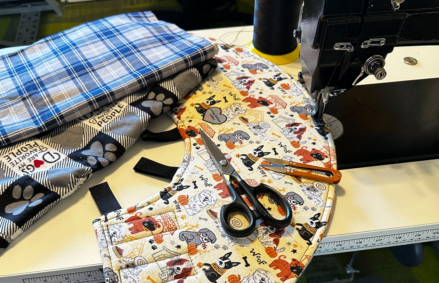 A stack of two different patterns of flannel fabric and a finished dog cone sit next to a sewing machine with Scissors and thread.